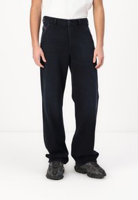 Marineblå denimbukser med lige snit, knaplukning og standard fem-lomme design. Båret med en hvid skjorte og mørke sneakers.
