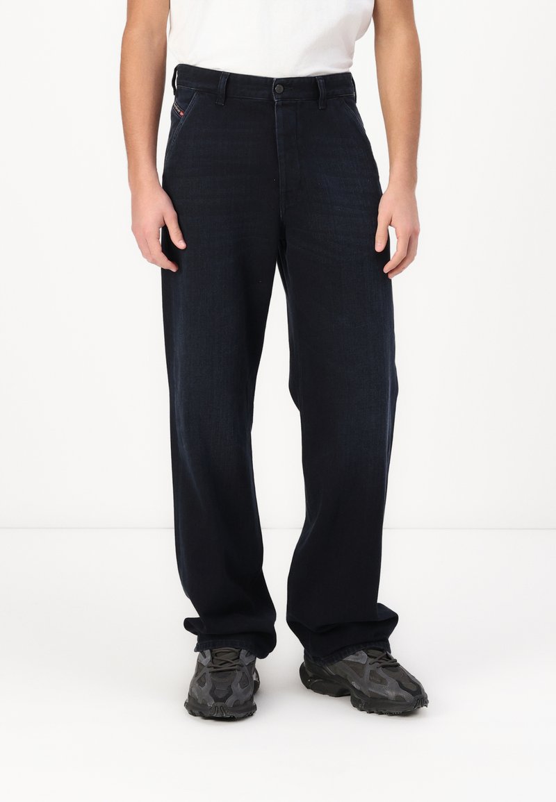 Marineblå denimbukser med lige snit, knaplukning og standard fem-lomme design. Båret med en hvid skjorte og mørke sneakers.