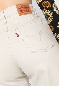 Levi's beige denimjeans med klassisk passform, som har en tan färgad läderpatch, en röd flik och en böjd design på bakfickan.