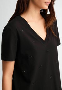 Tricou negru din bumbac, cu decolteu în V și mâneci scurte, decorat cu mici modele ovale cusute pe față.