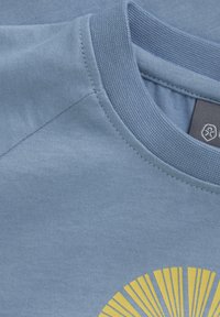 Ljusblå T-shirt med rundad halsringning. Har en gul solstrålesgrafik på nedre högra sidan. Mjuk bomullstyg med en jämn yta.