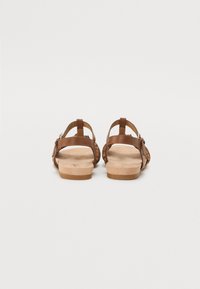 Brown leather sandals with cut-out design, two adjustable straps, and a natural-colored footbed, featuring a flat rubber sole.