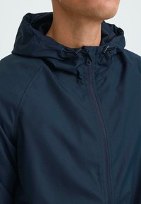 Navy windbreaker jacket with a hood, featuring a front zipper, adjustable drawstrings, and sleek, smooth fabric texture.