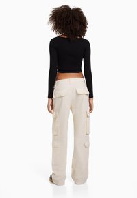 Černý žebrovaný cropped top v kombinaci se světle béžovými cargo kalhotami s několika kapsami a volným střihem, z pohledu zezadu.