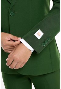 Giacca verde con rever a punta, quattro bottoni verdi e un dettaglio bianco sui polsi. Etichetta sulla manica con il logo "OPPO SUITS".