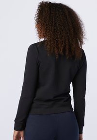 Maglione nero con maniche lunghe e scollatura rotonda, dotato di vita aderente e tessuto texture. Design semplice e minimalista.