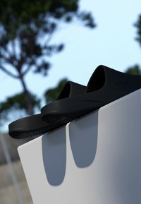 Black slide sandals made of rubber, featuring a smooth surface, open toe design, and textured sole with "LIGHTSTRIKE" branding on the side.