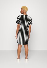 Vestido de manga curta com riscas brancas e pretas, cintura ajustada, bainha até ao joelho e uma textura de tecido suave. Ténis brancos usados como calçado.