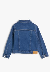 Chaqueta de mezclilla azul, con un cuello clásico, mangas largas con puños abotonados y una etiqueta beige en la parte baja de la espalda. Acabado de tejido texturizado.