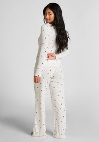 Conjunto de loungewear blanco de punto con un acabado texturizado, que presenta un patrón floral en negro y rojo. Parte superior de manga larga y pantalones acampanados.