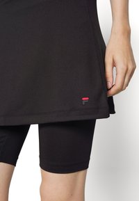 Falda atlética negra con pantalones cortos integrados, hecha de tejido elástico. Presenta un pequeño logo rojo y negro cerca del dobladillo lateral.