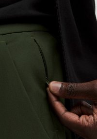 Rohelised püksid on varustatud tõmbluku taskuga, millel hoiab käsi tõmbluku. Kangas on sileda tekstuuriga ja sobib hästi keha vormiga.