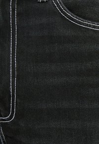 Jeans in denim nero con tessuto testurizzato, cuciture bianche a contrasto e dettagli sulle tasche, che mostrano un classico design a cinque tasche.