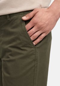 Pantalones de algodón verde oliva con bolsillos laterales y una textura suave, con costuras en contraste a lo largo de las costuras. Vista en primer plano de la zona de la cintura.