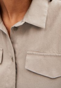 Chemise en lin gris clair avec un col, deux poches poitrine et des fermetures à boutons. Fabriquée dans un tissu texturé et respirant.