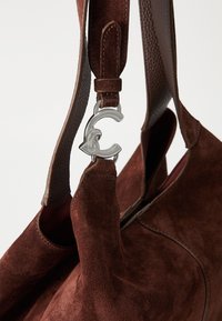 Ruskea mokkahandbag, jossa on sileä nahkahihna, hopeinen solki ja pehmeä, teksturoitu pinta.