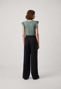 Lichtgroene top met gerimpelde mouwen, gecombineerd met zwarte wijde broek. Glad oppervlakte en een elastische tailleband op de broek.