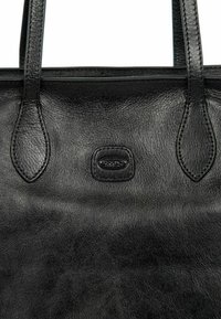 Zwarte leren tote bag met een gladde textuur, twee korte handvatten en een klein, reliëf logo aan de voorkant.