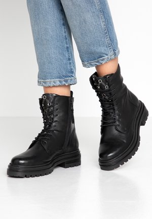 Botas de tobillo de cuero negro con punta redonda, diseño de cordones, cremalleras laterales y acentos texturizados. Suelas de goma gruesas y construcción resistente.
