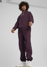 Mørkerød hættetrøje og joggers i struktureret stof, med et logo på brystet og benet, samt elastiske manchetter og snoretræk i hætten.