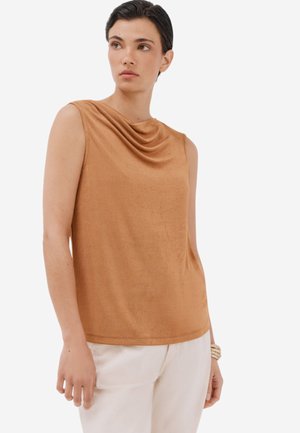 Top senza maniche di un caldo colore marrone, con scollatura drappeggiata, texture liscia e vestibilità comoda. Abbinato a pantaloni di colore chiaro.
