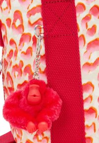 Portachiavi in peluche rosso a forma di gorilla, attaccato a uno zaino con un motivo a macchie di leopardo rosa e arancione e una tracolla rossa.