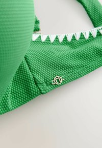Groen textuur bikini top met contrasterende witte zigzagafwerking en details van goudkleurig metalen op de zijkant. Voorzien van een gepadded bekerontwerp.