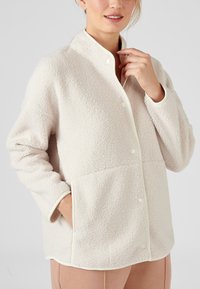 Vriendelijke beige fleece jas met een staande kraag, drukknoopsluiting, crèmekleurige bies en zijzakken, met een gestructureerd, zacht oppervlak.
