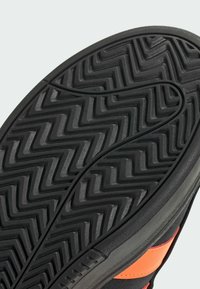 Suola di scarpa in gomma nera con un motivo a zigzag, caratterizzata da un bordo liscio e dettagli arancioni integrati nel design laterale.