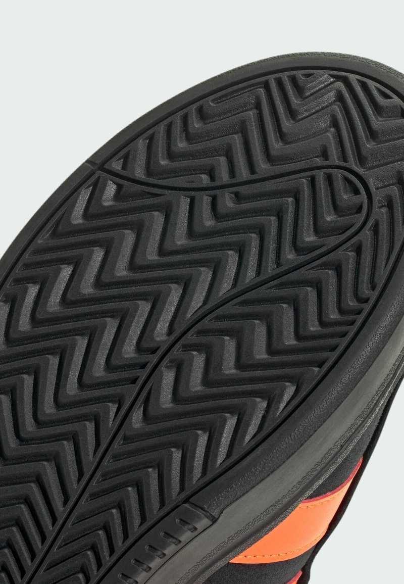 Semelle de chaussure en caoutchouc noir avec un motif de crampons en zigzag, dotée d'un bord lisse et d'accents orange intégrés dans le design latéral.