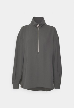 Tummanharmaa pitkähihainen pusero, jossa korkea kaulus ja hopeinen vetoketju, jonka vetopää on pyöreä, edessä keskellä, väljä istuvuus.