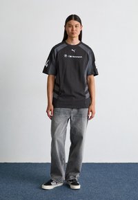 Harmaa lyhythihainen T-paita mustilla yksityiskohdilla ja logolla, yhdistetty haalistuneisiin harmaisiin farkkuihin ja mustiin skeittikenkäihin. Rentoon urheilulliseen tyyliin.