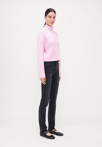 Pulover turtleneck roz, cu nervuri, cu mâneci lungi, asortat cu blugi negri cu croi drept și pantofi negri cu talpă plată, cu accente decorative.