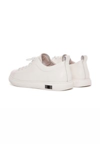 Sneakers in pelle bianca con finitura liscia, punta tonda, lacci bianchi piatti e un accento nero sul tallone; design minimalista.
