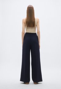 Wide-leg navy trousers with a smooth texture and tailored design, paired with a fitted beige tank top. No visible accents or patterns.