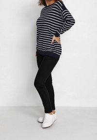 Navyblau-weiß gestreiftes Langarmoberteil mit lockerer Passform und gerippten Bündchen, kombiniert mit schwarzen Jeans und weißen Sneakers.