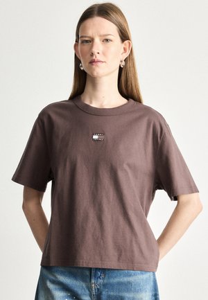 Brązowa bawełniana koszulka z luźnym krojem, okrągłym dekoltem i krótkimi rękawami. Posiada małą naszywkę z logo "TOMMY JEANS" na piersi.