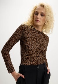 Top a maniche lunghe con stampa leopardata in marrone e nero, design aderente, tessuto morbido, scollatura a girocollo. Abbinato a pantaloni neri a vita alta.