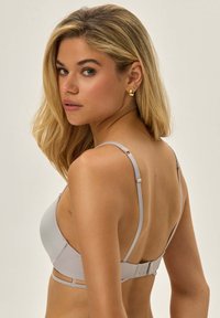 Jasnoszary biustonosz z gładkiego materiału, z regulowanymi ramiączkami i zapięciem na haftki. Charakteryzuje się niskim tyłem i minimalistycznym stylem.