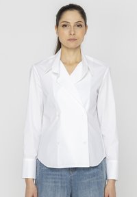 Biała, dwurzędowa koszula z wyłódkami, długimi rękawami i guzikami, w połączeniu z niebieskimi dżinsami. Gładka tekstura materiału.