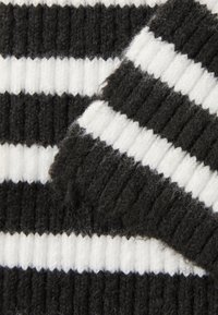 Tejido de punto a rayas blanco y negro con una textura acanalada, que presenta rayas alternas gruesas y finas. Superficie suave y ligeramente difusa.