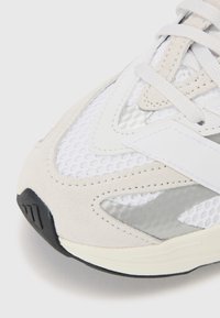 Baskets de sport gris clair avec une tige en mesh, des accents en daim, des détails réfléchissants argentés et une semelle en caoutchouc noir avec des motifs texturés.