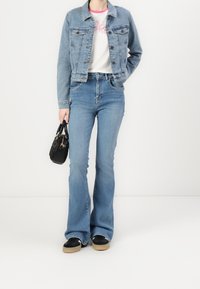 Jasnoniebieska kurtka dżinsowa o dopasowanym kroju. Biała koszula z różowymi akcentami, w połączeniu z dżinsami w wysokim stanie i szerokimi nogawkami oraz czarną torebką.