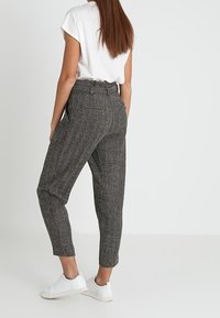 Pantalon grisé à texture, fuselé, taille haute avec poches latérales, associé à des baskets blanches et un haut blanc ample.
