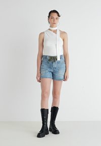 White asymmetrical top with a long tie, paired with high-waisted blue denim shorts and black knee-high lace-up boots.
