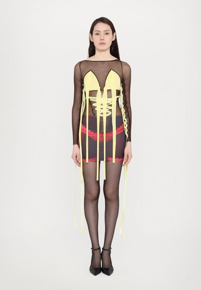 Robe noire transparente avec des rubans jaunes et des accents en dentelle rouge, présentant un décolleté plongeant et une coupe ajustée, assortie à des chaussures noires.