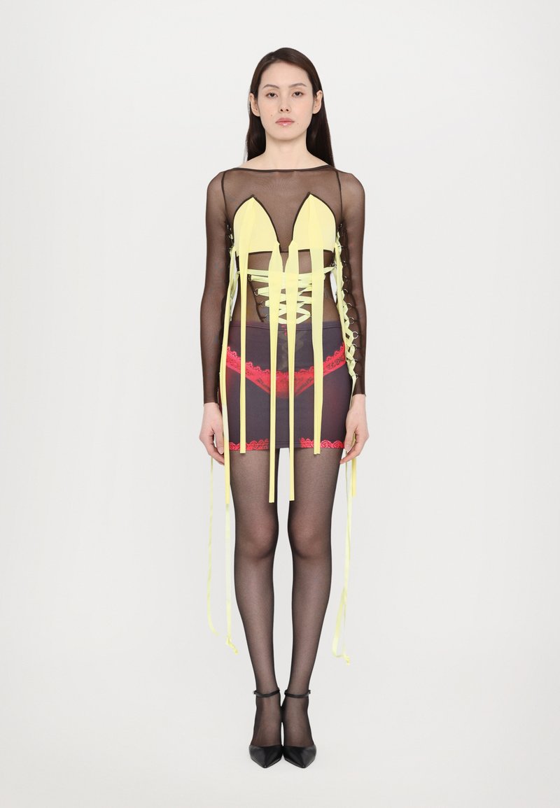 Transparentes schwarzes Kleid mit gelben Bändern und roten Spitzenakzenten, mit einem tiefen Ausschnitt und figurbetontem Design, kombiniert mit schwarzen Schuhen.