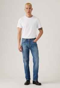 Witte katoenen t-shirt gecombineerd met blauwe denim jeans. Lichte wassing met een klassiek vijf-pocket ontwerp en zwarte enkellaarzen. Eenvoudige, rechte pasvorm.