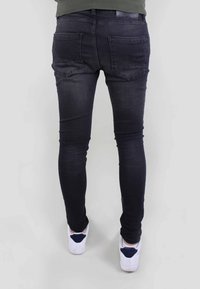 Jeans ajustados de color azul oscuro, fabricados en denim, con una textura suave, dos bolsillos traseros y un sutil detalle del logotipo en la cinturilla.