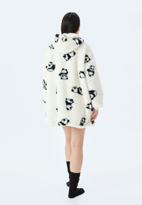 Sudadera blanca de felpa con patrones de osos panda negros, diseño oversize, textura suave y capucha. Las mangas son anchas y el dobladillo es ligeramente curvado.